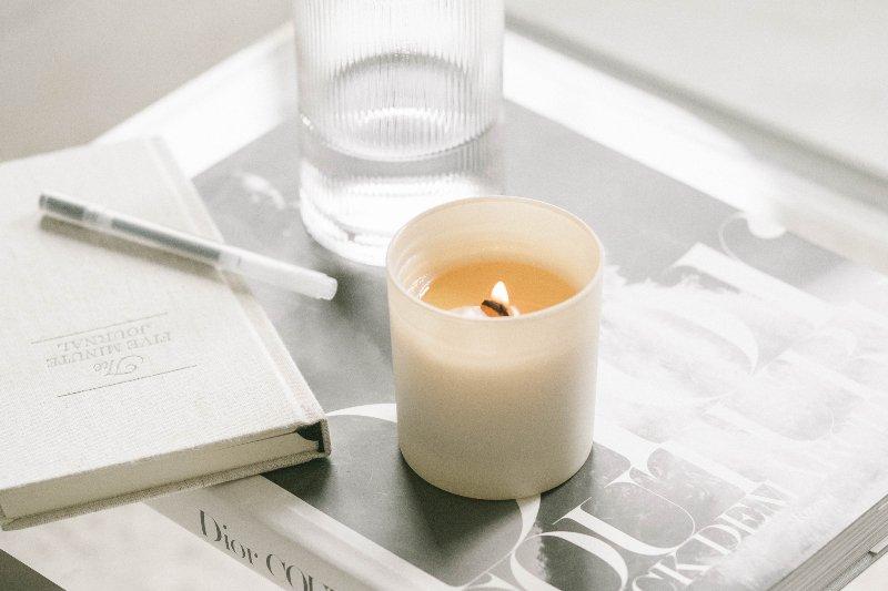 A photo of a Dior book with a candle, glass of water, and journal placed on top